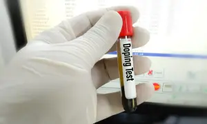 Rękawiczka trzyma probówkę z napisem "Doping Test". Wyniki badań na ekranie sugerują, czy testosteron jest legalny w sporcie.