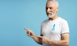 Starszy mężczyzna z niebieską wstążką na piersi, symbolizującą walkę z rakiem prostaty, wskazuje palcami w lewo. Dbałość o psa norma jest ważna.