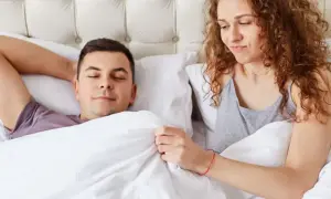 Kobieta z zaciekawieniem patrzy na śpiącego mężczyznę, zastanawiając się, dlaczego penis staje.