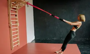 Kobieta wykonuje trening siłowy w domu dla początkujących, ćwicząc z taśmami TRX przy drabince gimnastycznej.