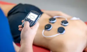 Osoba z pilotem steruje elektrodami na plecach. Trening EMS może przynieść korzyści, ale warto znać potencjalne trening ems skutki uboczne.
