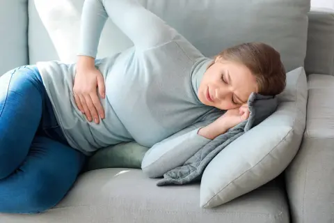 Kobieta z bólem brzucha szuka ulgi, wypróbowując na ból brzucha domowe sposoby.