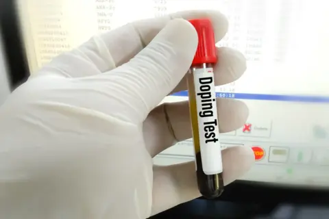 Rękawiczka trzyma probówkę z napisem "Doping Test". Wyniki badań na ekranie sugerują, czy testosteron jest legalny w sporcie.