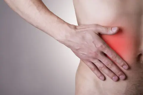 Mężczyzna trzyma rękę na boku, gdzie czerwony obszar sugeruje, że boli wątroba.