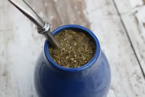 Niebieskie naczynie z yerba mate, gdzie liście unoszą się na wodzie. Choć yerba mate ma wiele zalet, warto pamiętać o jej negatywnych właściwościach, jak np. pobudzenie.