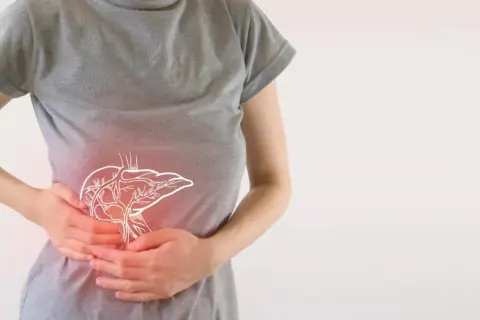 Osoba trzymająca się za brzuch, gdzie widoczny jest zarys wątroby. Może to symbolizować problemy trawienne lub skutki uboczne enzymów trawiennych.