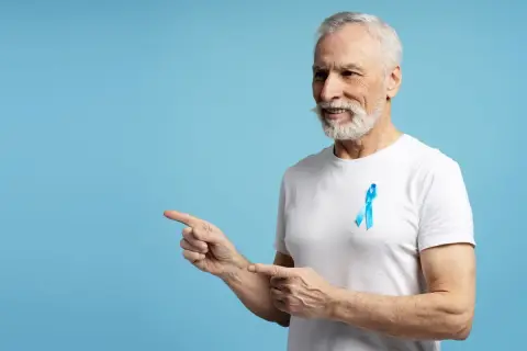 Starszy mężczyzna z niebieską wstążką na piersi, symbolizującą walkę z rakiem prostaty, wskazuje palcami w lewo. Dbałość o psa norma jest ważna.