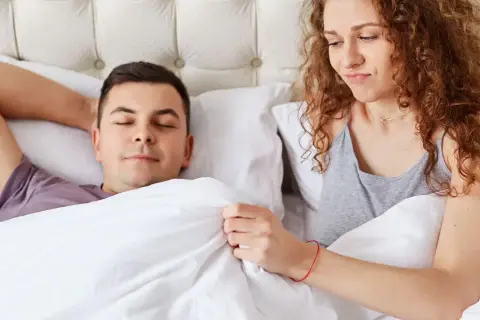 Kobieta z zaciekawieniem patrzy na śpiącego mężczyznę, zastanawiając się, dlaczego penis staje.