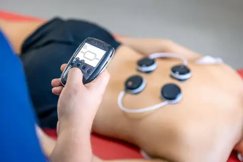 Osoba z pilotem steruje elektrodami na plecach. Trening EMS może przynieść korzyści, ale warto znać potencjalne trening ems skutki uboczne.